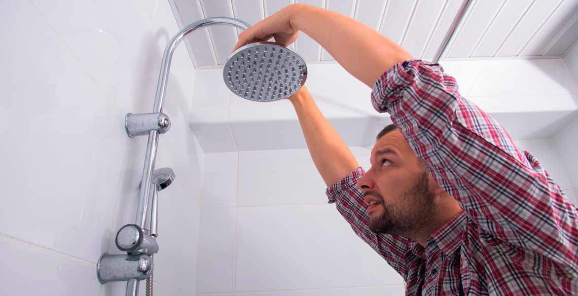 Un chico intentando reparar la cabeza de ducha en el baño de su casa