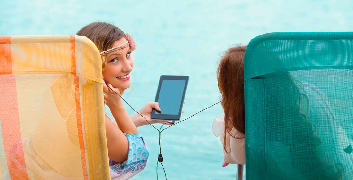 Dos mujeres jóvenes escuchando música en tableta digital mientras toman el sol en la playa